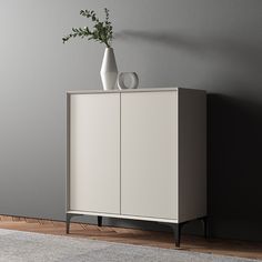 a white cabinet sitting on top of a wooden floor next to a vase with flowers