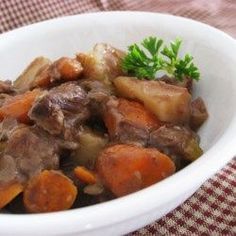 a white bowl filled with meat and carrots on top of a red checkered table cloth