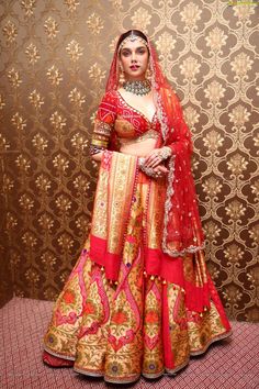 a woman in a red and gold bridal gown standing next to a golden wall