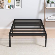 a black metal bed frame sitting on top of a hard wood floor next to a book shelf