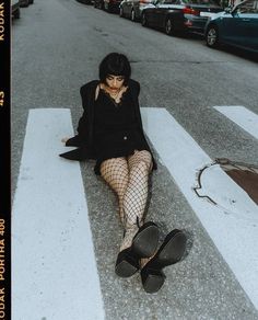 a woman in fishnet stockings and black shoes sitting on the street with her legs crossed