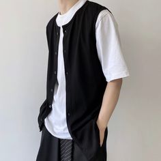 a young man wearing a black vest and white shirt standing in front of a wall