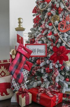 a christmas tree decorated with red, white and black plaid bows is surrounded by presents