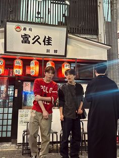 three young men are standing in front of a chinese restaurant with signs on the building