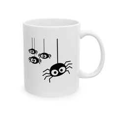 a white coffee mug with three black spideres hanging from it's webs