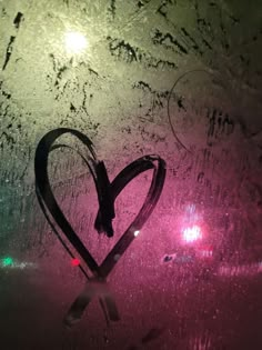 a heart drawn in the frosted glass on a rainy window with lights behind it