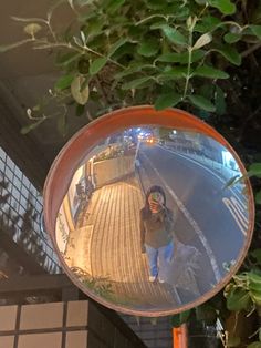 a mirror hanging from the side of a tree next to a building with a person walking on it