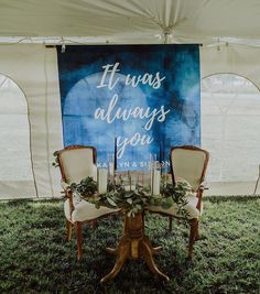 two chairs and a table with greenery on it under a large sign that says it was always you