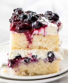 a close up of a piece of cake on a plate with blueberries and cream