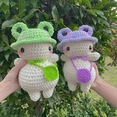 two crocheted stuffed animals are held up in front of a tree with leaves