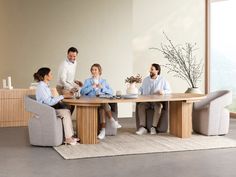 a group of people sitting around a wooden table in a living room next to a window