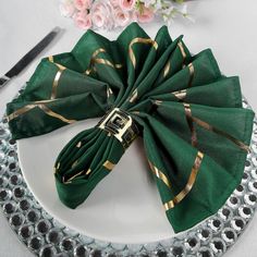 a green napkin with gold stripes on it sits on a plate next to a knife and fork