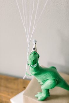 a green toy dinosaur with a party hat and balloons