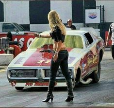 a woman in high heels standing next to a car with flames painted on the hood