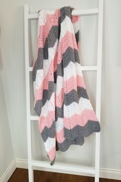 a pink and gray blanket hanging on a white ladder