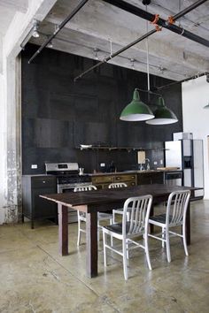 an industrial style kitchen and dining room with black walls, white chairs and green pendant lights