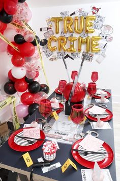 a table set up for a party with red and black plates, silverware and balloons