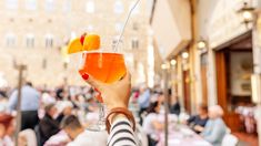 a woman holding up a glass filled with orange juice and an orange slice in it