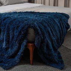 a bed with a blue blanket on top of it next to a wooden foot stool