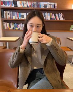 a woman sitting at a table drinking from a cup