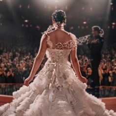 a woman in a white wedding dress walking down the runway at a fashion show with an audience behind her