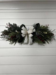 a christmas wreath hanging on the side of a white wall with pine cones and berries