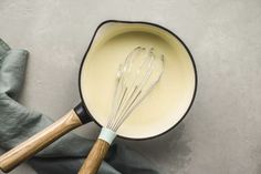 a whisk in a saucepan with two wooden spoons next to it