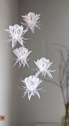 three white paper flowers hanging from strings in a room