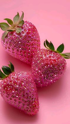 three pink strawberries with green leaves on a pink background