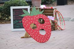 a wooden strawberry shaped sign sitting on top of a brick floor next to a chalkboard