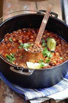 a pot filled with chili and beans on top of a blue towel next to a wooden table