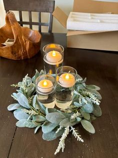 some candles are sitting on a table surrounded by greenery and other items in front of a wooden chair