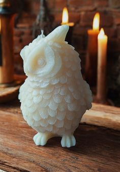 a white owl figurine sitting on top of a wooden table next to candles