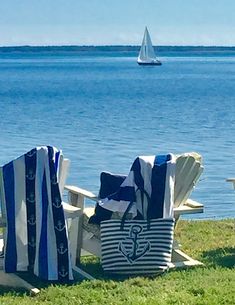 two beach chairs sitting next to each other in front of the ocean with a sailboat in the background