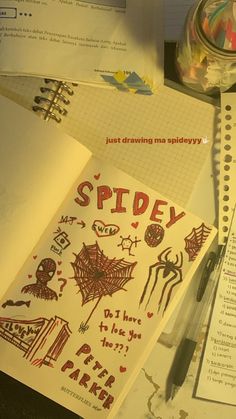 an open notebook sitting on top of a desk next to some papers and pens with spider drawn on them