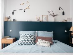 a bed with blue sheets and pillows in a bedroom next to a wall mounted clock