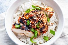 a white bowl filled with rice and meat covered in sesame seeds, scallions and green onions