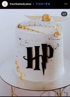 a white cake with black letters and gold decorations on the top is sitting on a table