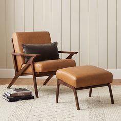 a chair and ottoman in a living room with white walls, rugs and books on the floor