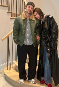 two people standing next to each other in front of a stair case with a coat on