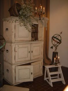 an old dresser with flowers on top and candles in the bottom, next to a ladder