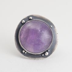 "This all sterling silver ring features a round amethyst, set on a recycled silver backplate, studded with small silver balls. The ring shank is about 8mm wide. The face of the ring is about 1.25\" x 1.25\" across. The ring has been oxidized and selectively brushed to highlight the details. The ring is US size 8.5. It can be enlarged on request in quarter sizes up to 9.5. Because of the width of the band, I'd suggest ordering a size 1/4 to 1/2 larger than normal. Please read my shipping and poli Sterling Silver Purple Ring With Large Stone, Purple Amethyst Ring With Sterling Silver, Purple Amethyst Ring In Sterling Silver, Sterling Silver Amethyst Ring With Large Stone, Purple Amethyst Ring With Round Stone In Sterling Silver, Unique Silver Amethyst Ring With Large Stone, Sterling Silver Cabochon Amethyst Ring, Nickel-free Silver Amethyst Ring In Sterling Silver, Sterling Silver Amethyst Cabochon Ring