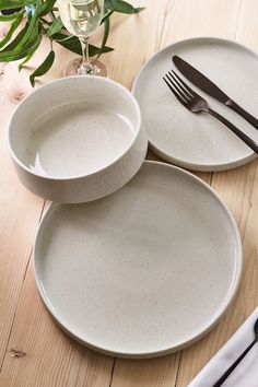 three white plates with black handles on a wooden table next to silverware and flowers