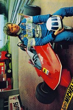 a man sitting on top of a red motor scooter in a garage next to a wall