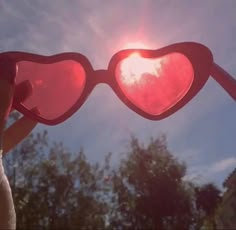 someone holding up two heart shaped glasses in front of the sun with trees behind them