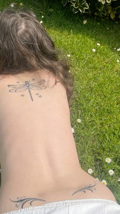 a man with a dragonfly tattoo on his back is laying down in the grass