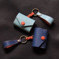 two leather key fobs are laying on a black surface, one is blue and the other is orange