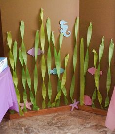 some paper fish and seaweed are on the wall next to a purple table cloth