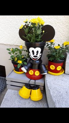 mickey mouse planter with yellow flowers in it and other potted plants next to it