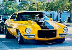 a yellow muscle car with a black stripe on it's hood parked in a parking lot